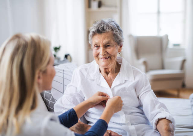 A health visitor helping a sick senior woman sitting on bed at home.